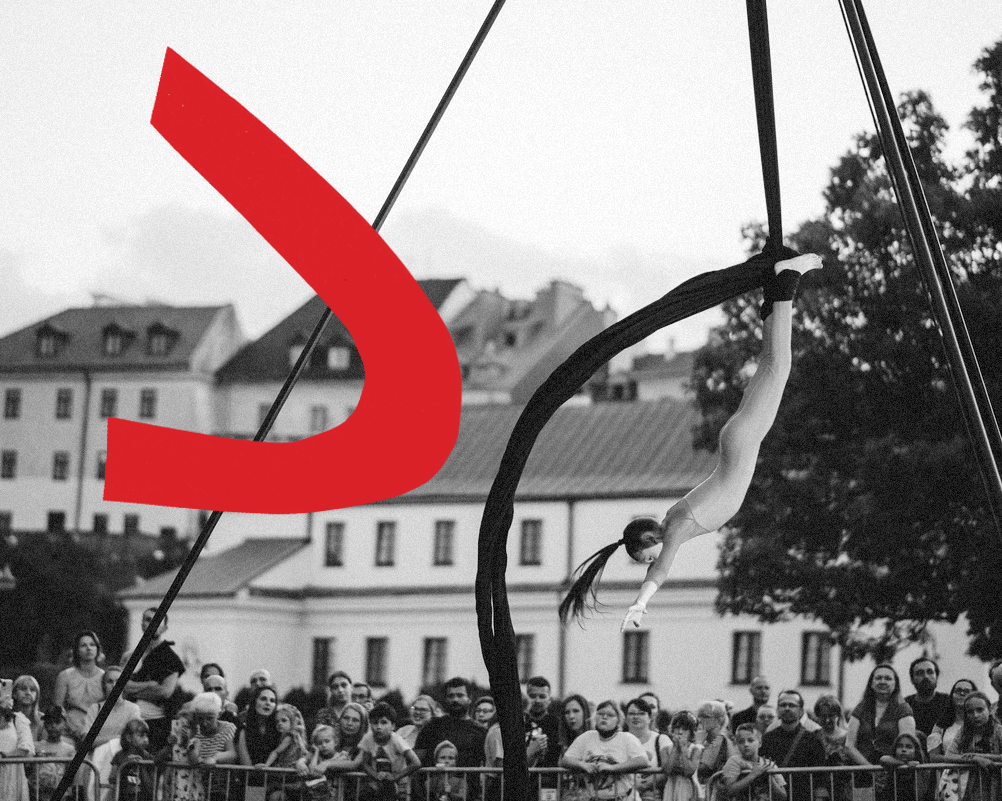 Fotografia czarno-biała. Akrobartka wisi głową w dół na placu Litewskim.