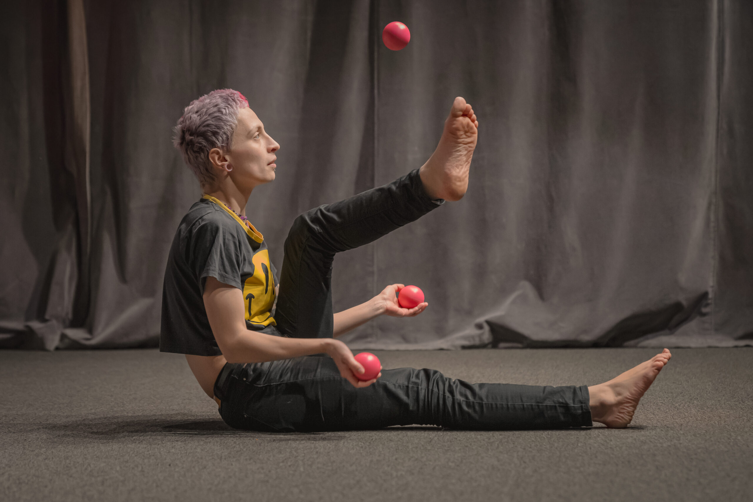 Kobieta żongluje piłeczkami nad swoją nogą.