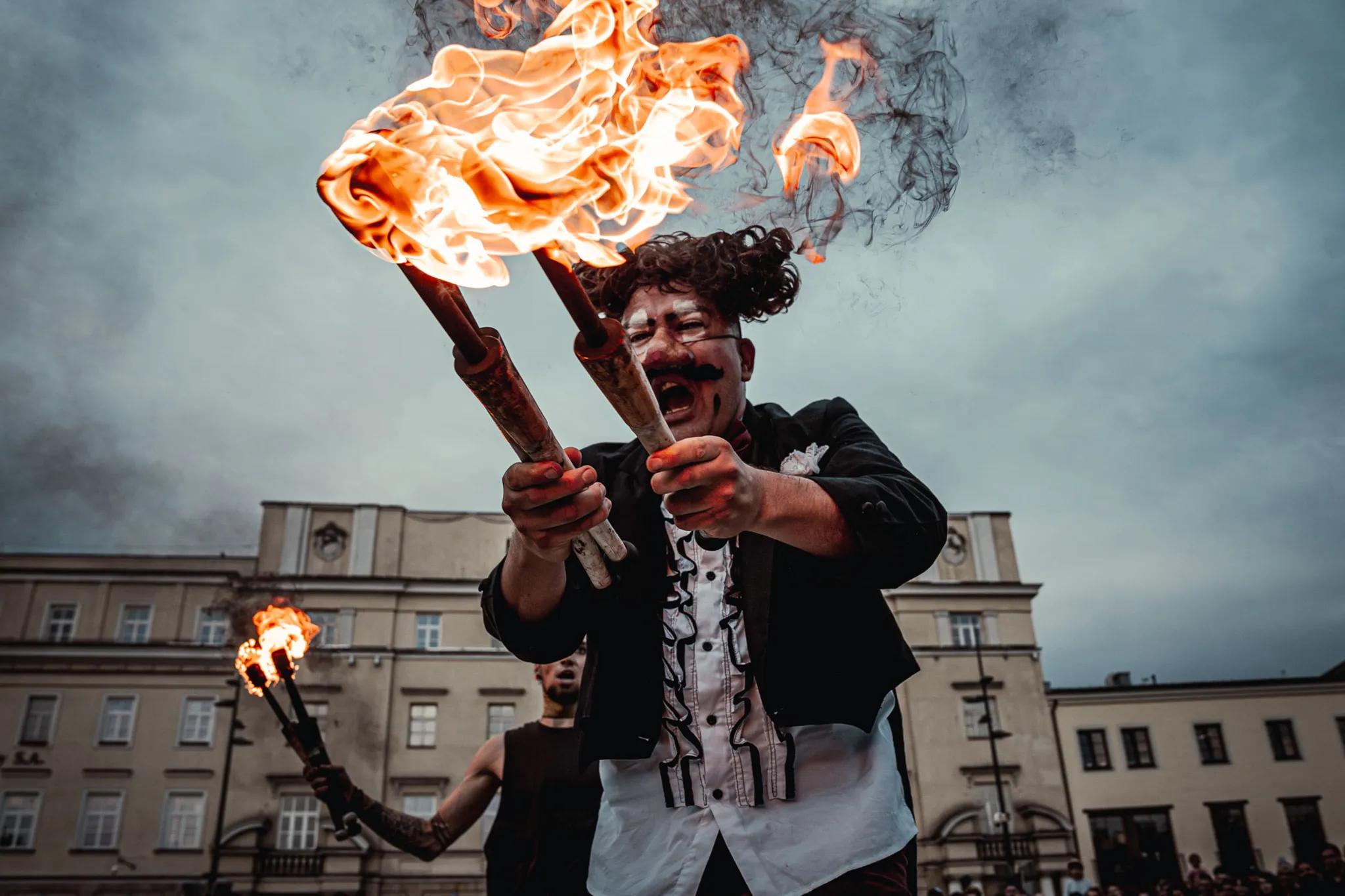 Clown trzyma w rękach dwie palące się pochodnie.